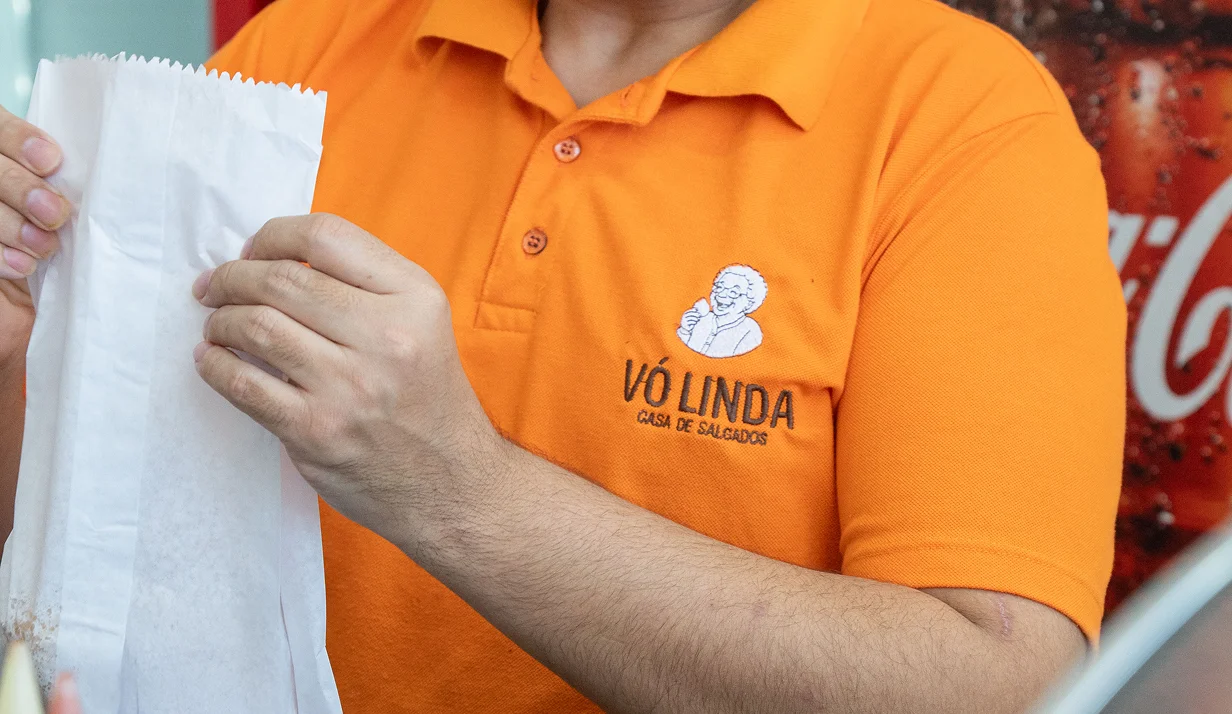 Funcionário da Vó Linda Casa de Salgados embalando salgados frescos em saquinho de papel para entrega